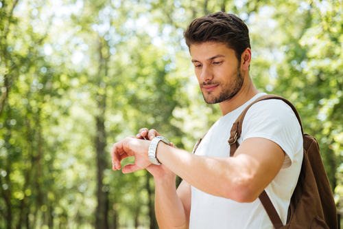 Man backpacking on trail checking his wristwatch.