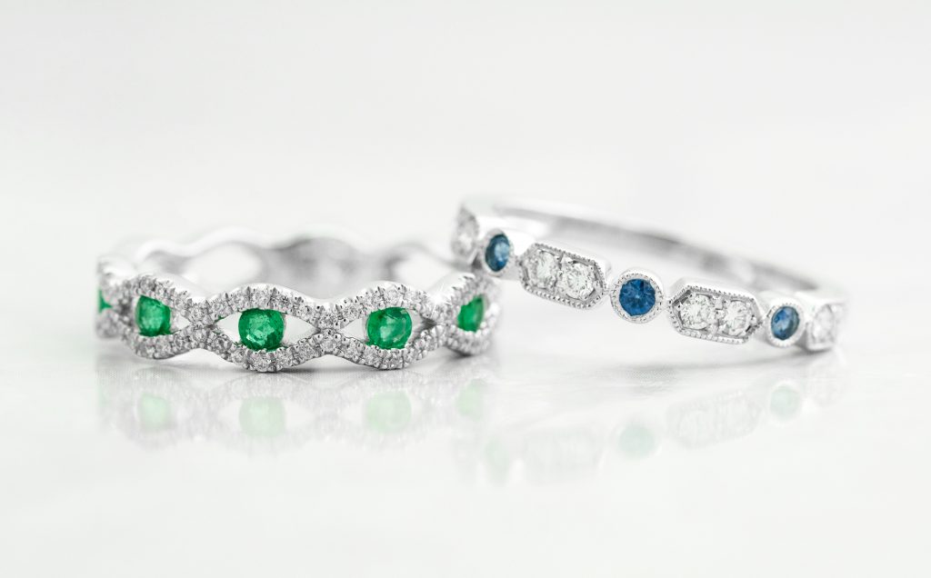 White gold wedding bands, one set with emeralds and diamonds and the other set with blue sapphires and diamonds.