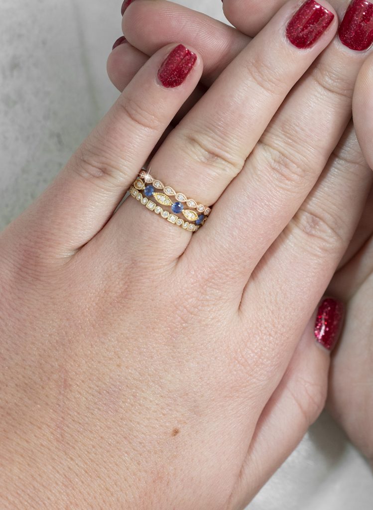 Woman wearing three yellow gold diamond and emerald stackable eternity rings.