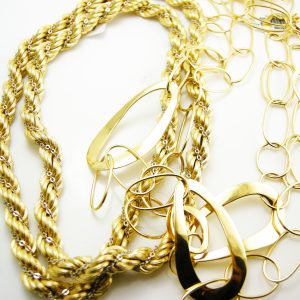 Yellow gold chains, earrings and bracelets, stacked on a white table.