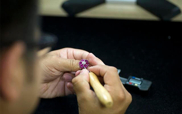 Jeweler checking for loose stones on a gemstone ring at their bench.