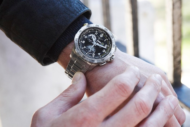 Man’s wrist featuring a pre-owned men’s Hamilton Khaki Chrono Worldtimer in stainless steel with a black dial, yellow and white markers, and stainless-steel bracelet.