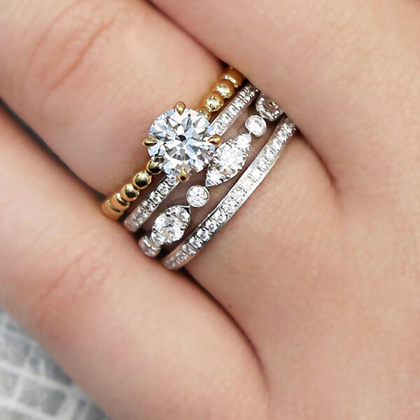 Yellow gold diamond engagement ring stacked with three white gold diamond eternity
bands on woman’s finger.