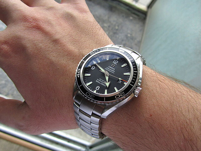 Man’s wrist featuring an Omega Seamaster in stainless steel with a black dial and bezel.