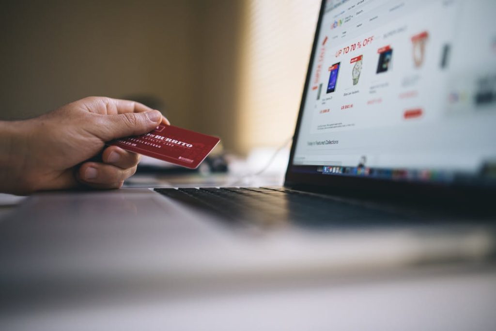 A person holding a red credit card while shopping online on a laptop, with discounts and product listings visible on the screen.