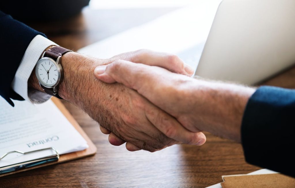 Two men in suits shaking hands while one of them wears watch on wrist.