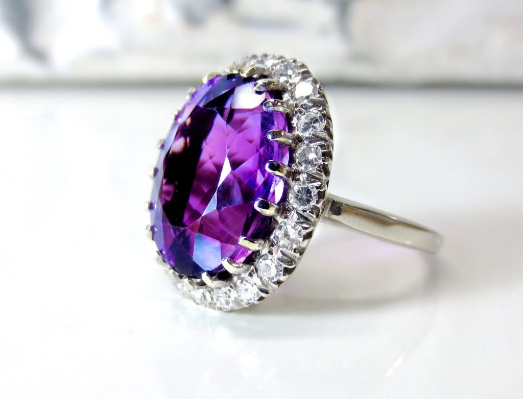 White gold ring centered with a purple gemstone surrounded by a diamond halo.