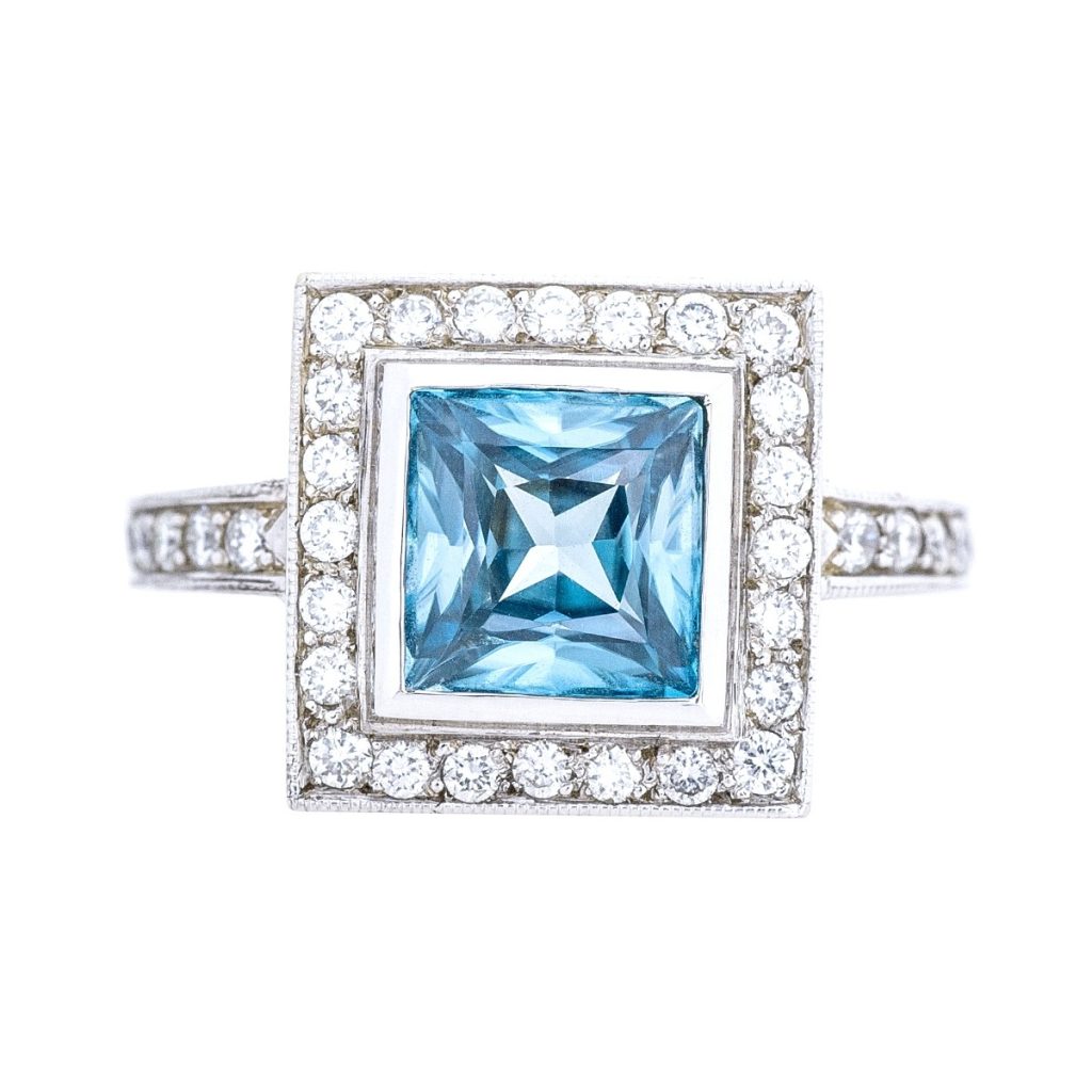 White gold engagement ring centered with blue zircon surrounded by a diamond halo and
diamonds in the band.