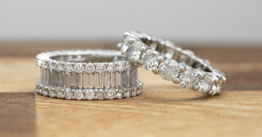 Two white gold diamond eternity bands on a wooden table.