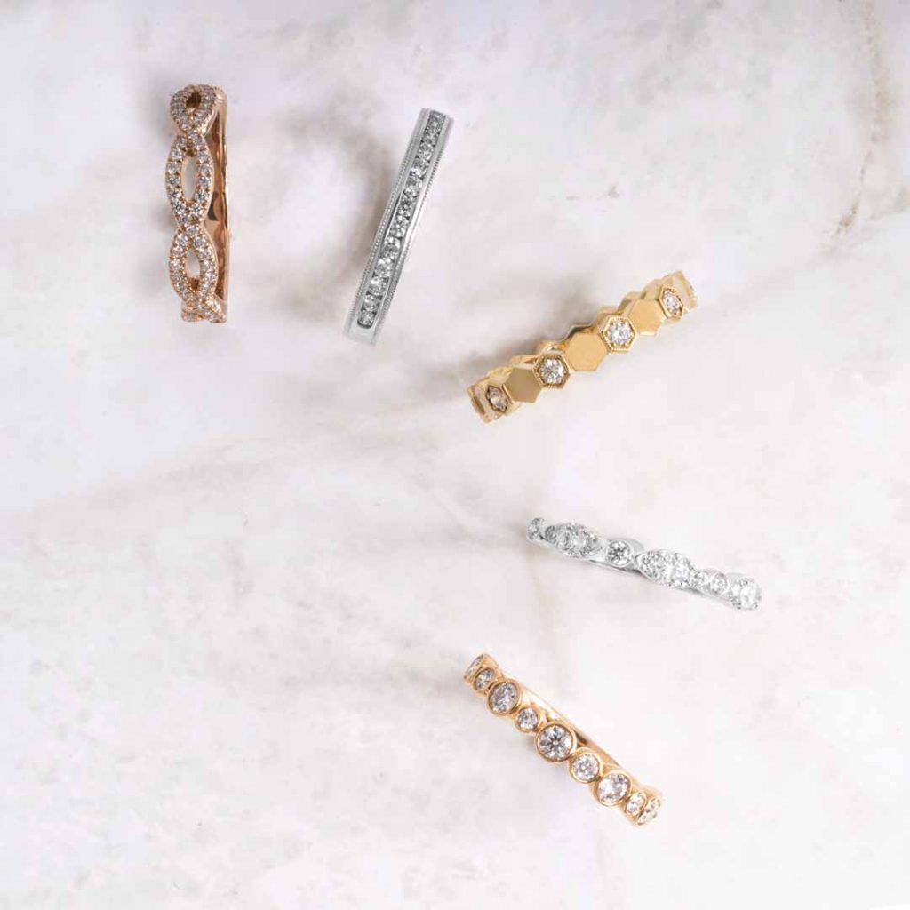 Five diamond wedding bands in various metals on a marble table.