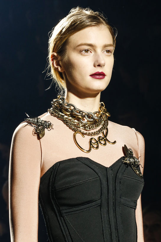 Runway model wearing several layered statement yellow gold necklaces.