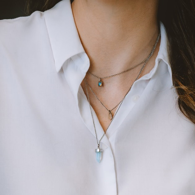 Woman in white button-up wearing three layered pedant necklaces.