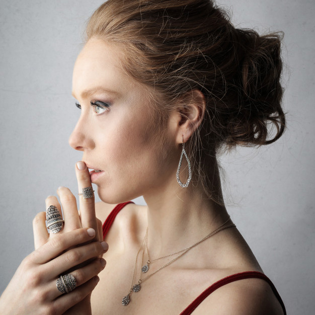 Woman wearing stacked rings, layered necklaces, and drop earrings.