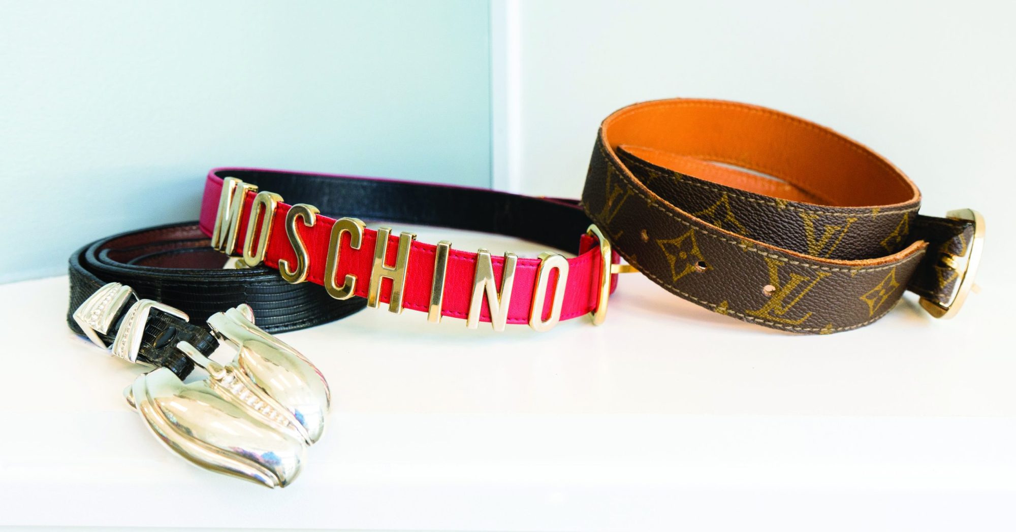 Three vintage designer belts on a white table.