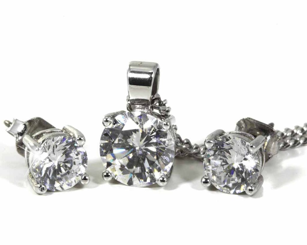 Diamond stud earrings and a matching solitaire pendant necklace set in white gold, featuring round-cut stones in prong settings.