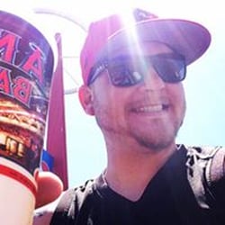 A smiling man wearing sunglasses and a red cap, holding a large cup.