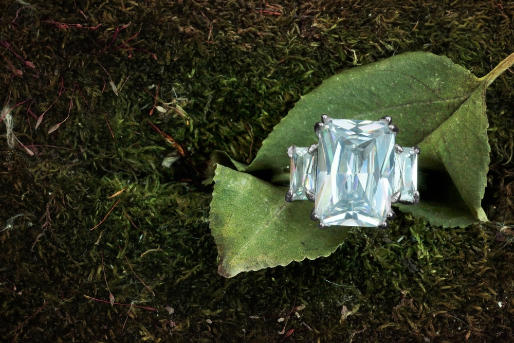 White gold three-stone colored diamond engagement ring on a leaf.