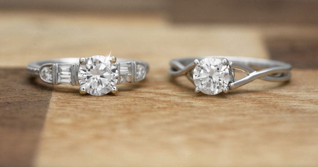 Two white gold diamond engagement rings on a wooden table.