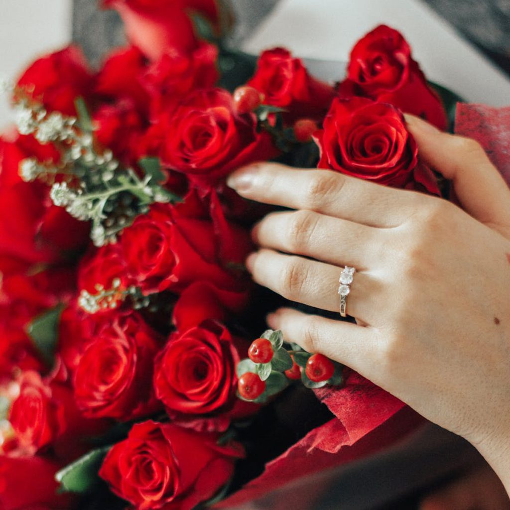 Woman’s hand in red rose bouquet showing off her diamond engagement ring.