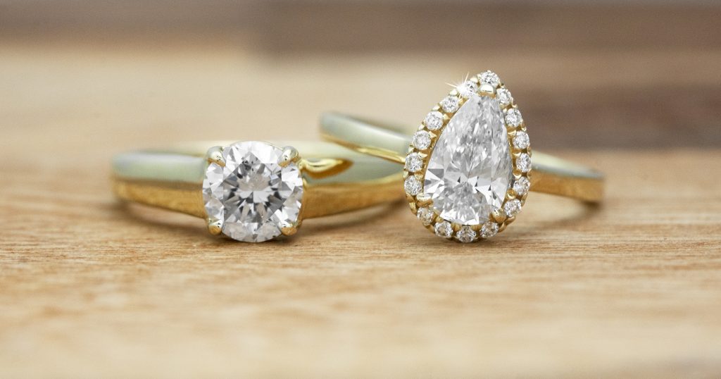 Two yellow gold diamond engagement rings on a wooden table.