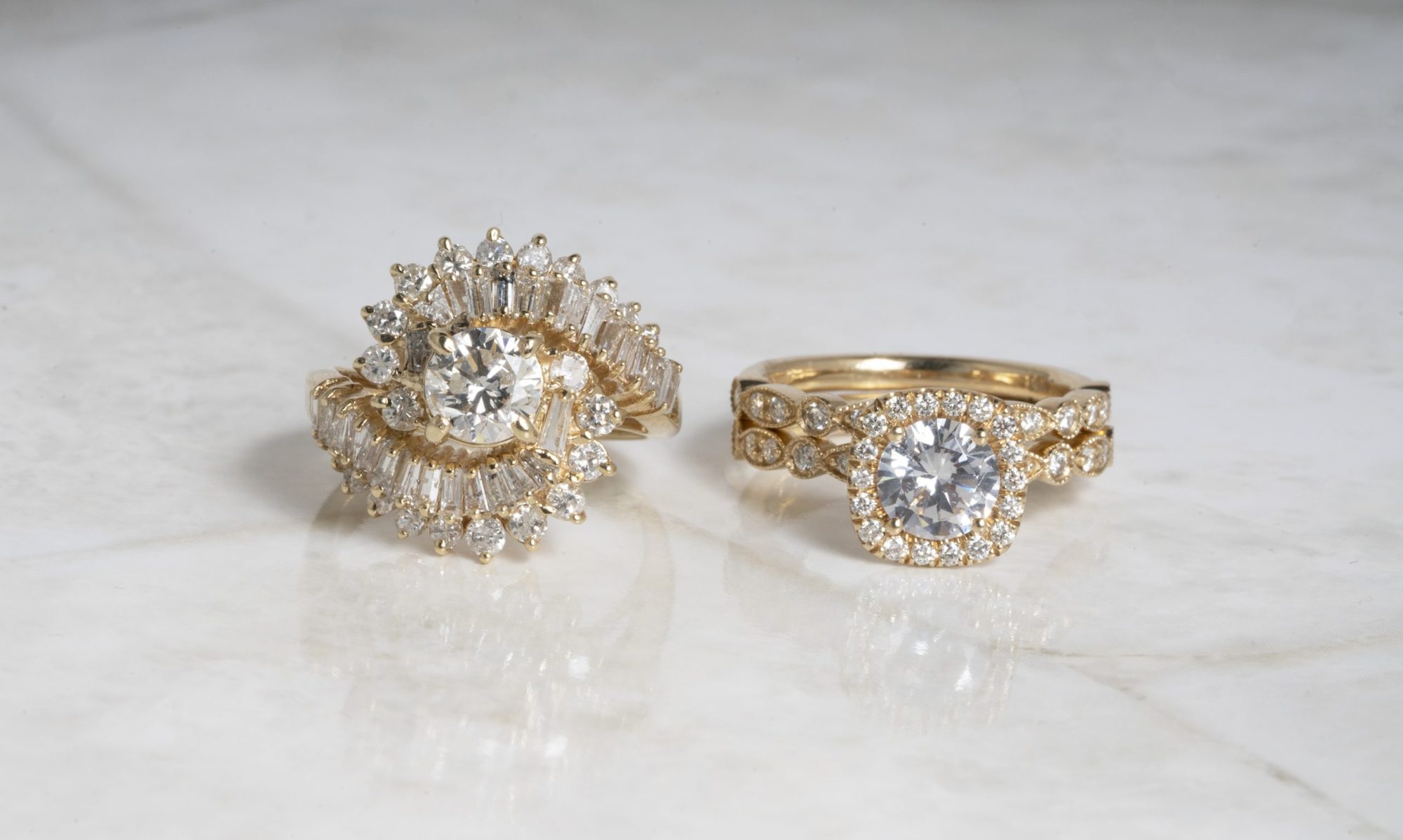 Two yellow gold diamond engagement rings both with diamonds surrounding the centers.